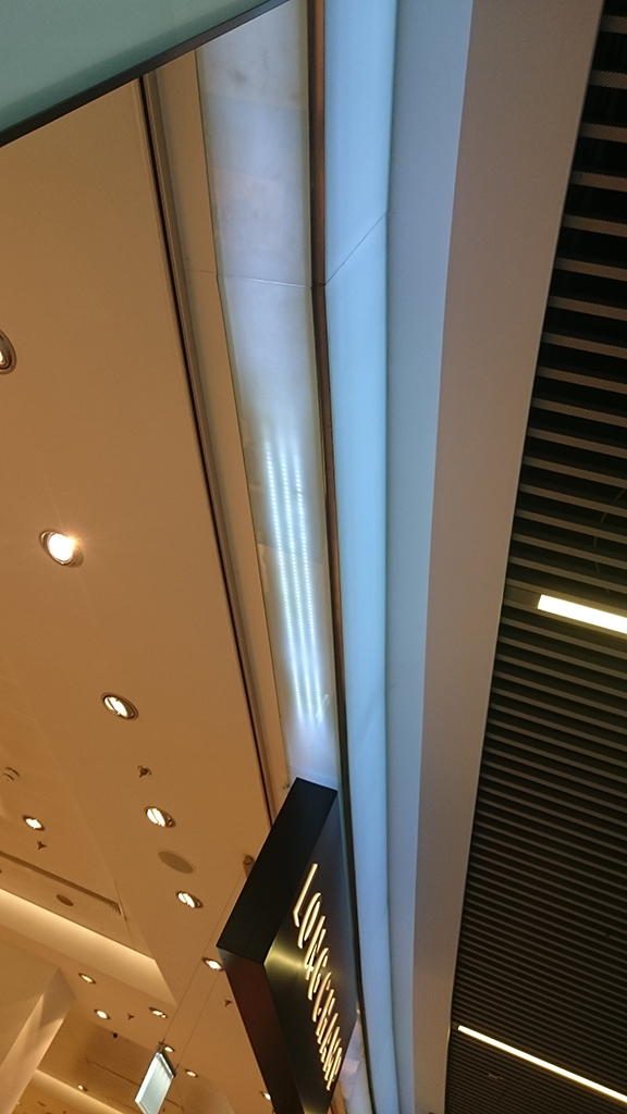 Üvegburkolat és világítástechnika kombinációja, sík és ívelt üvegburkolatok a SkyCourtban. A fénysávok közrefogják az üzletek portáljait.