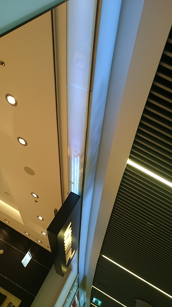 Üvegburkolat és világítástechnika kombinációja, sík és ívelt üvegburkolatok a SkyCourtban. A fénysávok közrefogják az üzletek portáljait.